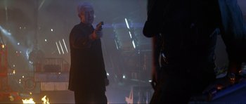 Movie still from “Tomorrow Never Dies” (1997), directed by Roger Spottiswoode – An older man holding a cell phone in his hand; Medium shot, Over the shoulder angle