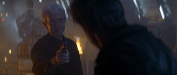 Movie still from “Tomorrow Never Dies” (1997), directed by Roger Spottiswoode – An older man holding a gun in front of a mirror; Close Up shot, Over the shoulder angle