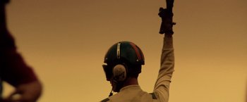 Movie still from “Top Gun” (1986), directed by Tony Scott – A person wearing a helmet raising their hand; Medium shot, Low angle