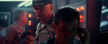 Movie still from “Top Gun” (1986), directed by Tony Scott – A man in a military uniform is standing next to another man; Close Up shot, Low angle