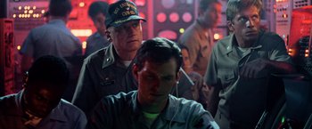 Movie still from “Top Gun” (1986), directed by Tony Scott – A man with headphones and a man in a military uniform; Medium shot, Over the shoulder angle