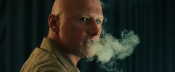 Movie still from “Top Gun” (1986), directed by Tony Scott – A bald man is smoking a cloud of smoke in front of a mirror; Close Up shot, Low angle