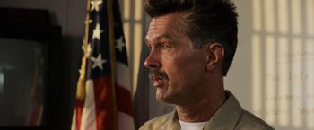 Movie still from “Top Gun” (1986), directed by Tony Scott – An older man with a mustache and a flag in the background; Close Up shot, Low angle