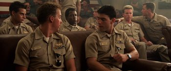 Movie still from “Top Gun” (1986), directed by Tony Scott – A group of men sitting next to each other on top of a couch; Medium shot, Over the shoulder angle