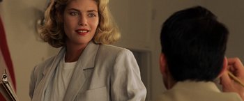 Movie still from “Top Gun” (1986), directed by Tony Scott – A woman wearing a white jacket talking to a man in a tan suit; Close Up shot, Over the shoulder angle