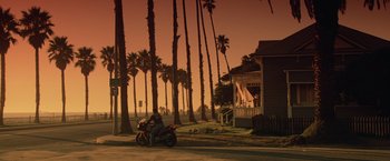 Movie still from “Top Gun” (1986), directed by Tony Scott – A motorcycle parked on the side of the road near palm trees; Extreme Wide shot, Low angle