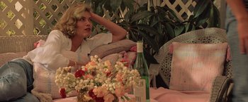Movie still from “Top Gun” (1986), directed by Tony Scott – A woman sitting at a table with a bottle of wine and flowers; Medium shot, Low angle