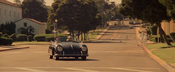 Movie still from “Top Gun” (1986), directed by Tony Scott – An old car driving down a street past trees; Wide shot, High angle