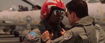 Movie still from “Top Gun” (1986), directed by Tony Scott – A man wearing a helmet and sunglasses is putting on a jacket; Close Up shot, Low angle