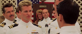 Movie still from “Top Gun” (1986), directed by Tony Scott – A group of people in military uniforms in front of a flag; Close Up shot, Over the shoulder angle