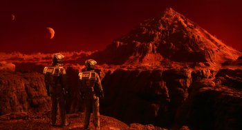 Movie still from “Total Recall” (1990), directed by Paul Verhoeven – Two people in space suits standing in front of a red mountain; Extreme Wide shot, High angle