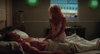 Movie still from “Total Recall” (1990), directed by Paul Verhoeven – A man laying on a bed with a woman standing next to him; Wide shot, High angle
