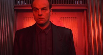 Movie still from “Total Recall” (1990), directed by Paul Verhoeven – A man wearing a suit and tie standing in front of a red wall; Close Up shot, Low angle