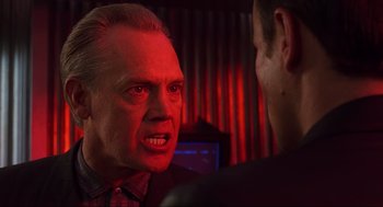 Movie still from “Total Recall” (1990), directed by Paul Verhoeven – A man in a red shirt is talking to another man in front of a computer screen; Close Up shot, Over the shoulder angle