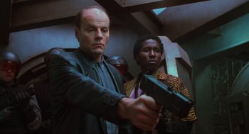 Movie still from “Total Recall” (1990), directed by Paul Verhoeven – A man holding a gun while standing next to another man; Medium shot, Low angle