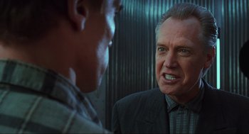 Movie still from “Total Recall” (1990), directed by Paul Verhoeven – A man in a suit and tie talking to another man in a suit and tie; Close Up shot, Over the shoulder angle