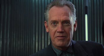 Movie still from “Total Recall” (1990), directed by Paul Verhoeven – An older man in a suit and tie looking at the camera; Close Up shot, Low angle