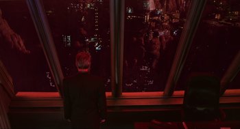 Movie still from “Total Recall” (1990), directed by Paul Verhoeven – A man standing in front of a window looking out at a city at night; Wide shot, High angle
