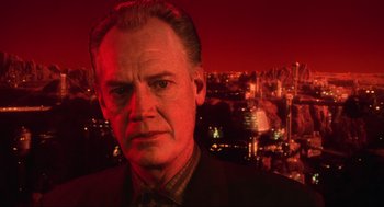 Movie still from “Total Recall” (1990), directed by Paul Verhoeven – A man in a suit and tie in front of a city skyline; Close Up shot, Low angle