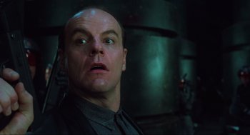 Movie still from “Total Recall” (1990), directed by Paul Verhoeven – A bald man with a black shirt is looking at the camera; Close Up shot, Low angle