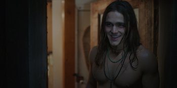 Movie still from “Totally Killer” (2023), directed by Nahnatchka Khan – A man with long hair and a necklace smiling; Medium shot, Over the shoulder angle