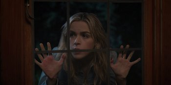 Movie still from “Totally Killer” (2023), directed by Nahnatchka Khan – A woman looking through a window with her hands up; Medium shot, Over the shoulder angle