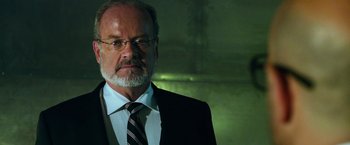 Movie still from “Transformers: Age of Extinction” (2014), directed by Michael Bay – A man in a suit and tie standing in front of a wall; Close Up shot, Low angle