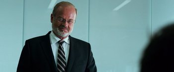 Movie still from “Transformers: Age of Extinction” (2014), directed by Michael Bay – A man in a suit and tie standing in front of a glass wall; Close Up shot, Over the shoulder angle