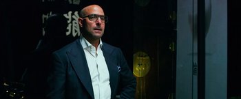 Movie still from “Transformers: Age of Extinction” (2014), directed by Michael Bay – A man in a suit and glasses standing in front of a wall; Close Up shot, Low angle