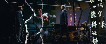 Movie still from “Transformers: Age of Extinction” (2014), directed by Michael Bay – A man in a suit walking in front of a screen; Wide shot, Over the shoulder angle