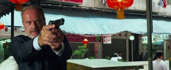 Movie still from “Transformers: Age of Extinction” (2014), directed by Michael Bay – A man in a suit holding a gun in front of a building; Medium shot, Low angle