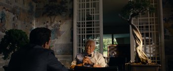 Movie still from “Transformers: Dark of the Moon” (2011), directed by Michael Bay – An older man sitting at a table in front of a television; Medium shot, Over the shoulder angle