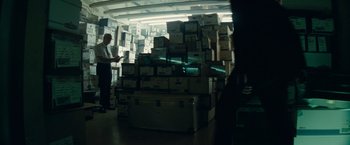 Movie still from “Transformers: Dark of the Moon” (2011), directed by Michael Bay – A man standing in front of a large stack of boxes; Wide shot, Over the shoulder angle