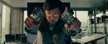 Movie still from “Transformers: Dark of the Moon” (2011), directed by Michael Bay – A man in a suit and glasses holding two pistols in his hands; Close Up shot, Low angle