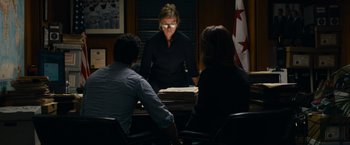 Movie still from “Transformers: Dark of the Moon” (2011), directed by Michael Bay – Three people sitting at a table in front of a flag; Medium shot, Over the shoulder angle