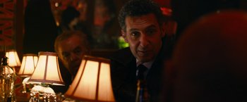 Movie still from “Transformers: Dark of the Moon” (2011), directed by Michael Bay – A person sitting at a table near a lamp; Close Up shot, Over the shoulder angle