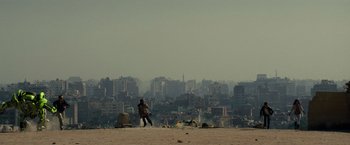 Movie still from “Transformers: Revenge of the Fallen” (2009), directed by Michael Bay – A man standing on top of a sandy beach near a city; Extreme Wide shot, High angle