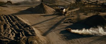 Movie still from “Transformers: Revenge of the Fallen” (2009), directed by Michael Bay – An orange truck driving down a dirt road next to piles of gravel; Extreme Wide shot, High angle