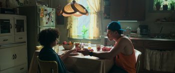 Movie still from “Transformers: Rise of the Beasts” (2023), directed by Steven Caple Jr. – Two people sitting at a dining room table with a bowl of fruit on the table; Medium shot, Over the shoulder angle