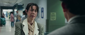 Movie still from “Transformers: Rise of the Beasts” (2023), directed by Steven Caple Jr. – A woman in a beige jacket is sitting in a room; Close Up shot, Over the shoulder angle