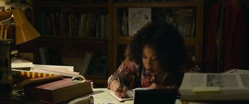 Movie still from “Transformers: Rise of the Beasts” (2023), directed by Steven Caple Jr. – A woman writing on a piece of paper in front of an open book; Medium shot, High angle