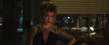 Movie still from “Transformers: Rise of the Beasts” (2023), directed by Steven Caple Jr. – A woman in a gold and black dress looking at the camera; Medium shot, Over the shoulder angle