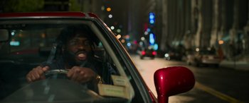 Movie still from “Transformers: Rise of the Beasts” (2023), directed by Steven Caple Jr. – A man sitting in the drivers seat of a red car; Close Up shot, Low angle