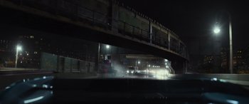 Movie still from “Transformers: Rise of the Beasts” (2023), directed by Steven Caple Jr. – A car driving under an overpass at night; Extreme Wide shot, High angle