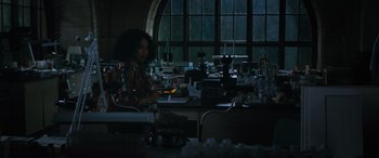 Movie still from “Transformers: Rise of the Beasts” (2023), directed by Steven Caple Jr. – A woman sitting at a table in front of a window; Medium shot, Low angle