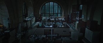 Movie still from “Transformers: Rise of the Beasts” (2023), directed by Steven Caple Jr. – Two people working in a lab in front of a large window; Extreme Wide shot, High angle