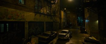 Movie still from “Transformers: Rise of the Beasts” (2023), directed by Steven Caple Jr. – Two cars are parked in an alleyway at night; Extreme Wide shot, High angle