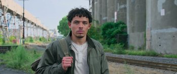 Movie still from “Transformers: Rise of the Beasts” (2023), directed by Steven Caple Jr. – A young man with a backpack standing on the side of the road; Close Up shot, Low angle