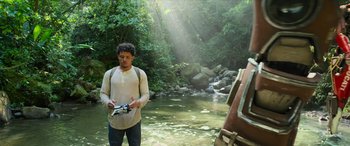 Movie still from “Transformers: Rise of the Beasts” (2023), directed by Steven Caple Jr. – A man holding a camera in front of a river; Wide shot, Low angle