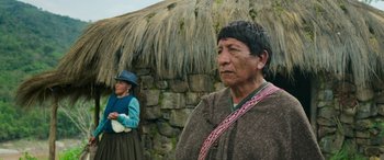 Movie still from “Transformers: Rise of the Beasts” (2023), directed by Steven Caple Jr. – Two people standing in front of a thatched hut; Medium shot, Over the shoulder angle